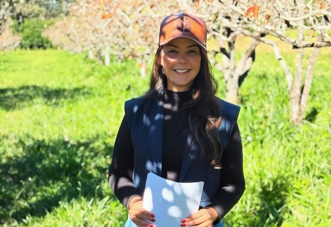 Bruna sorrindo num pomar, com o diagnóstico da propriedade nas mãos